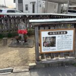 赤い前掛けをかけた木抱かれ地蔵と、その説明板