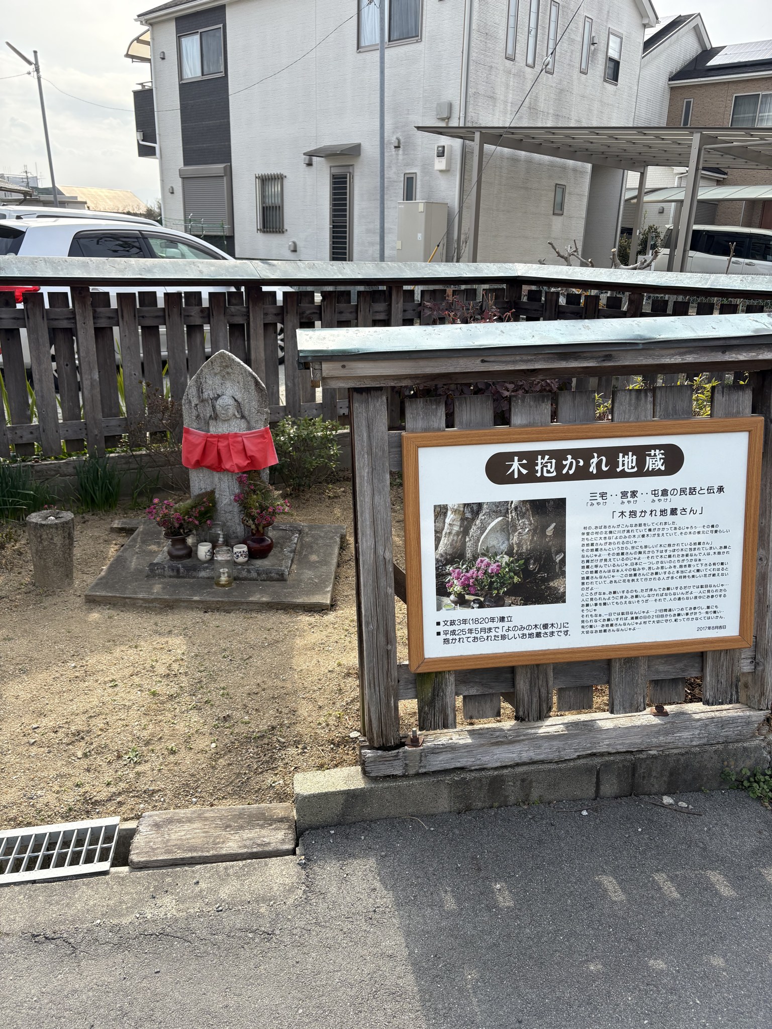 赤い前掛けをかけた木抱かれ地蔵と、その説明板