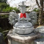 赤い前掛けをした壷阪寺の千手観音石像と桜